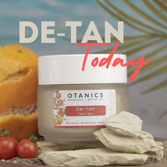 Image of Otanics De-Tan Face Pack jar with a white lid and a clear label. The label reads 'Otanics De-Tan Face Pack' with a red and yellow background and illustrations of tomatoes and citrus fruits. The jar is placed on a textured surface, surrounded by natural elements like stones, with the bold text 'DE-TAN Today' displayed above. The product is cruelty-free, 100% natural, and vegan as indicated on the label.